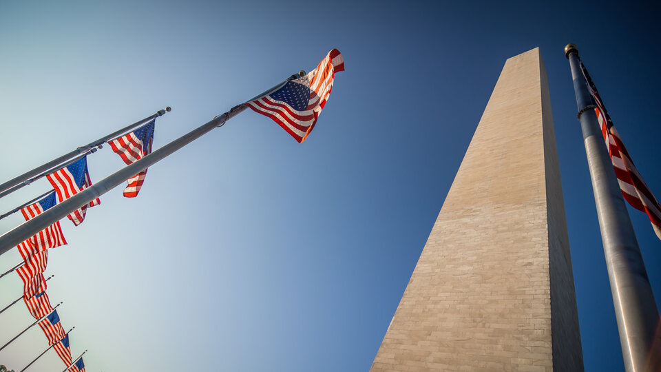 Looking up from underneath the Washington Monument, surrounded by American flags