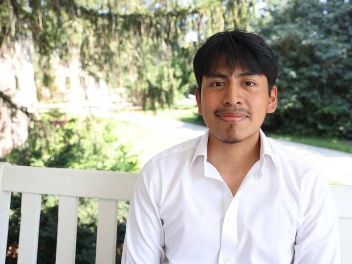 Man in a white shirt sitting on a bench in a sunny, green park.