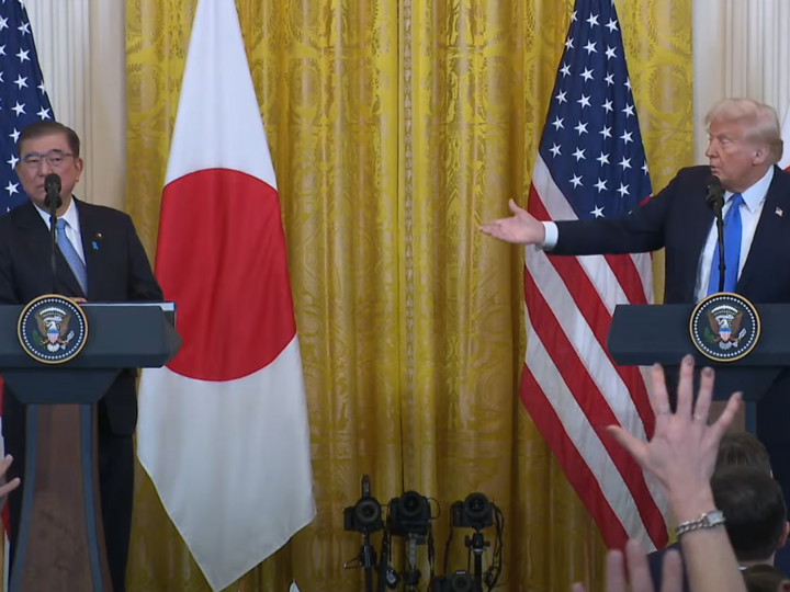 Japanese Prime Minister Ishiba standing on stage, behind a podium, with US President Trump, who is also behind a podium. Trump has right hand pointing in the direction of Japanese Prime Minister.