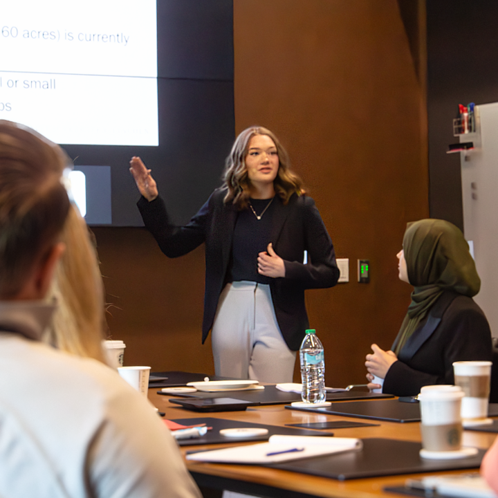 Alexis Bodlak speaking in front of a table to a group of people